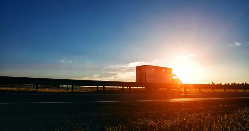 A box truck drives on the highway at sunset